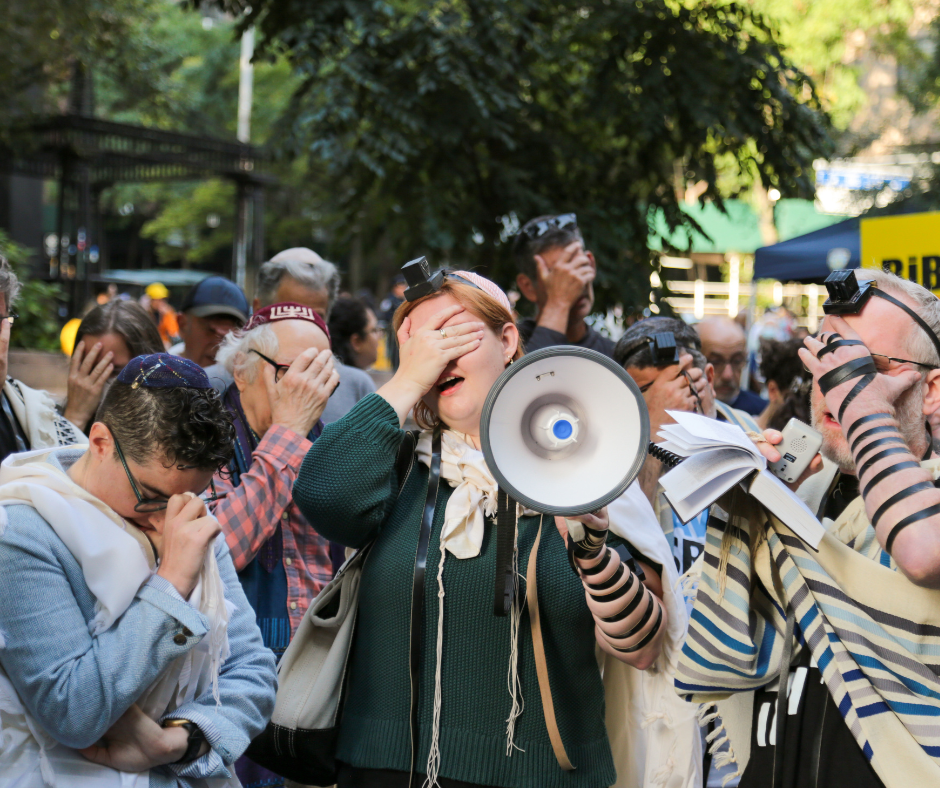 Three rabbis at a protest wearing tallitot cover their eyes for the shema prayer.