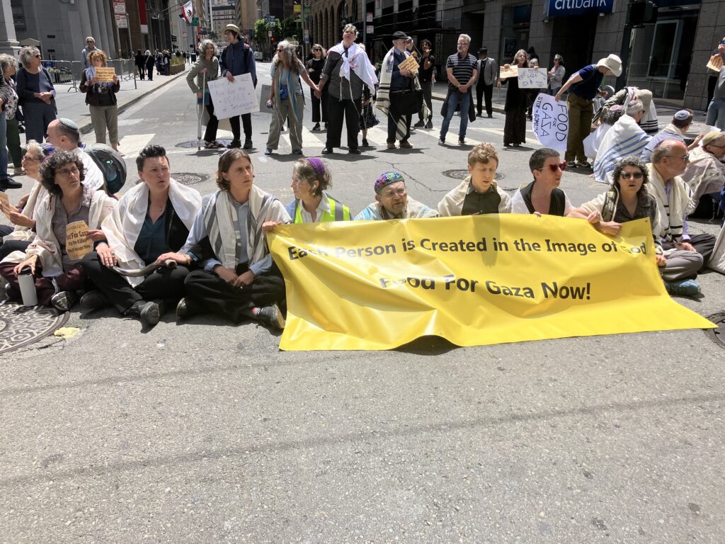 Rabbis sit in a row in street holding a sign that says food for gaza now.
